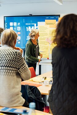zwei Menschen stehend mit dem Blick auf die Dozierende