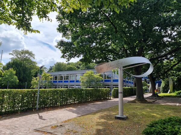 Bild vergrößern: Außenansicht des Gebäudes der Johannes-Brahms-Schule mit Skulptur und Baum im Vordergrund