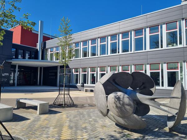 Bild vergrößern: Außenansicht des Gebäudes der Theodor-Heuss-Schule mit Skulptur im Vordergrund